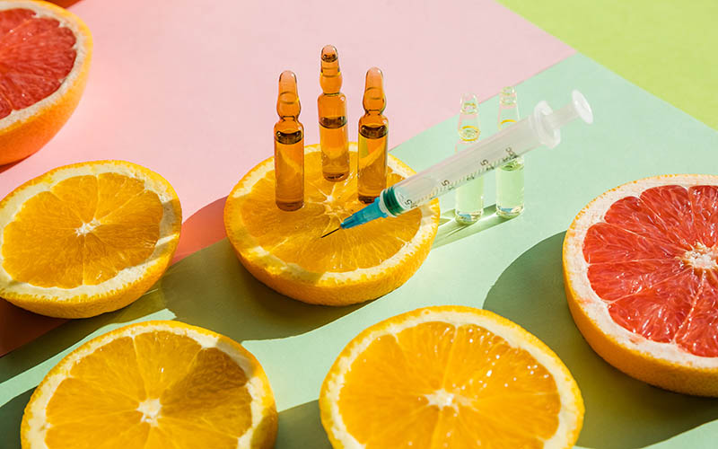 High dose vitamin C, ampule for injection with syringe and fresh juicy orange fruit slides. Concept of vitamin,mineral supplement, beauty.