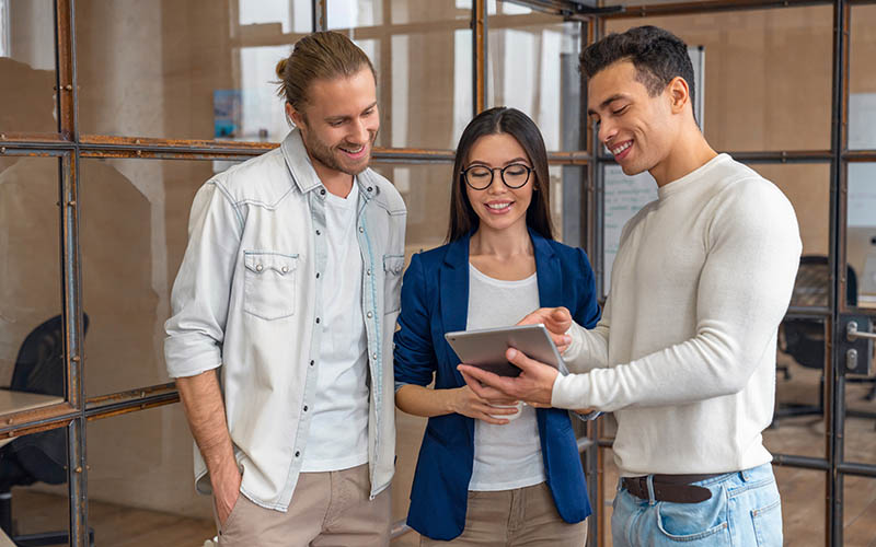 Three young business professionals standing together and discussing over business report in office hallway. Office colleagues revieving a business document on the tablet in coworking